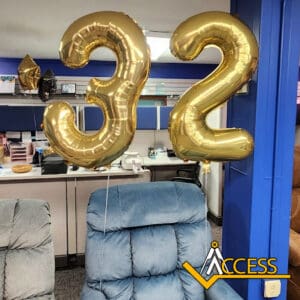 Two large gold balloons shaped like the number 32 are floating above blue chairs in an office space. The logo ACCESS is displayed in the bottom right corner of the image.