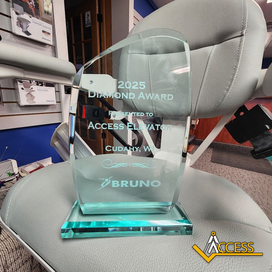 A glass award engraved with “2025 Diamond Award presented to Access Elevator, Cudahy, WI, Bruno” is displayed on a gray chair, with the Access company logo visible in the bottom right corner.
