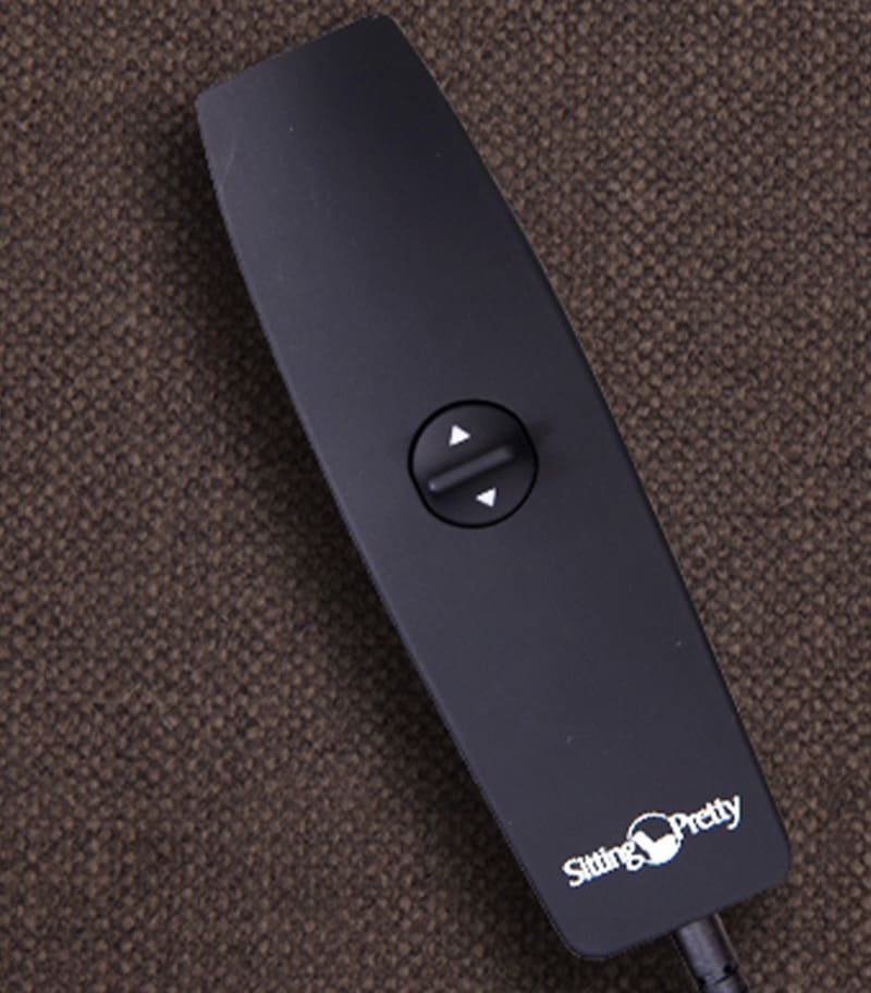 A black remote with two arrow buttons and "Sitting Pretty" rests on brown fabric, designed for use with the Evolution (LC-435) Lift Chair by Pride Mobility. A black remote with two arrow buttons and "Sitting Pretty" rests on brown fabric, designed for use with the Evolution (LC-435) Lift Chair by Pride Mobility.