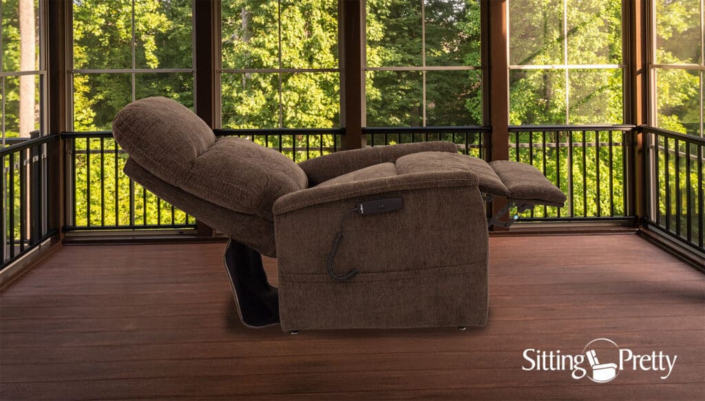 A Genesis LC-150 Lift Chair by Pride Mobility in brown sits on a wooden floor in a bright sunroom with large windows and views of green trees. "Sitting Pretty" appears in the lower right corner.