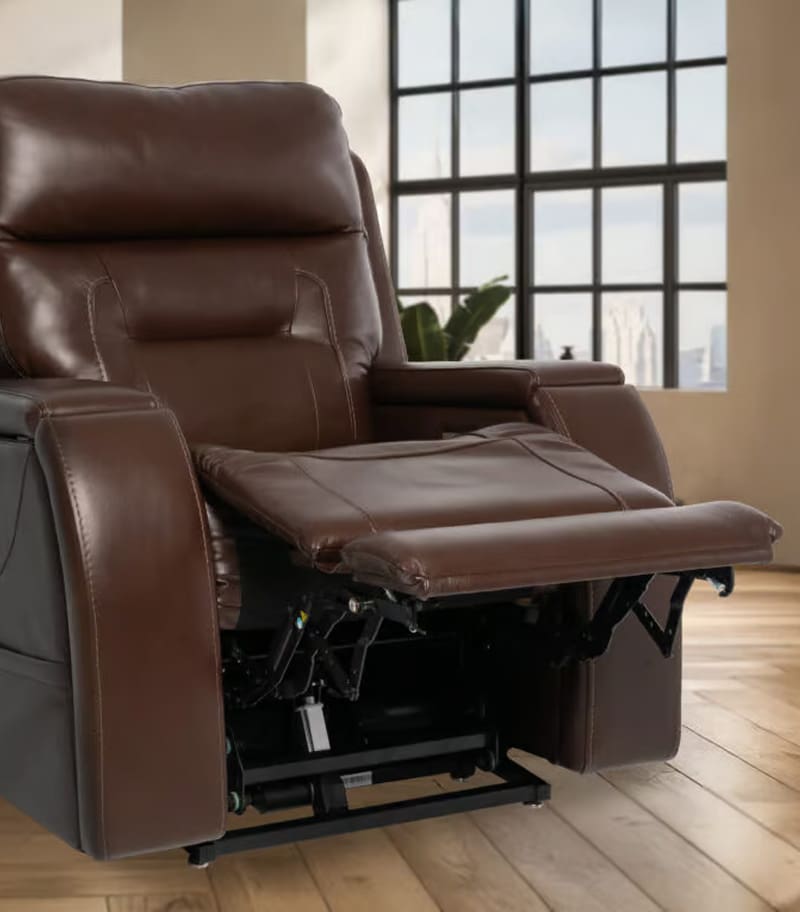 The VivaLift Premier PLR-5900 Lift Chair by Pride Mobility, upholstered in brown leather with the footrest extended, sits on a wooden floor in a sunlit room featuring large windows. The VivaLift Premier PLR-5900 Lift Chair by Pride Mobility, upholstered in brown leather with the footrest extended, sits on a wooden floor in a sunlit room featuring large windows.
