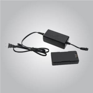 A black electronic power adapter with an attached cable and plug is placed next to a rectangular black battery on a plain gray background.