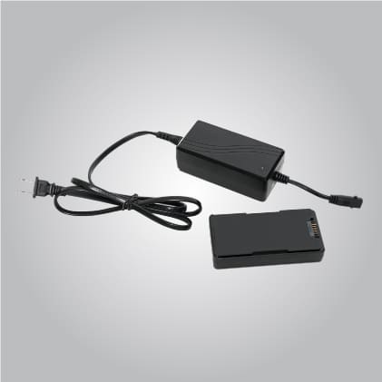 A black electronic power adapter with an attached cable and plug is placed next to a rectangular black battery on a plain gray background.