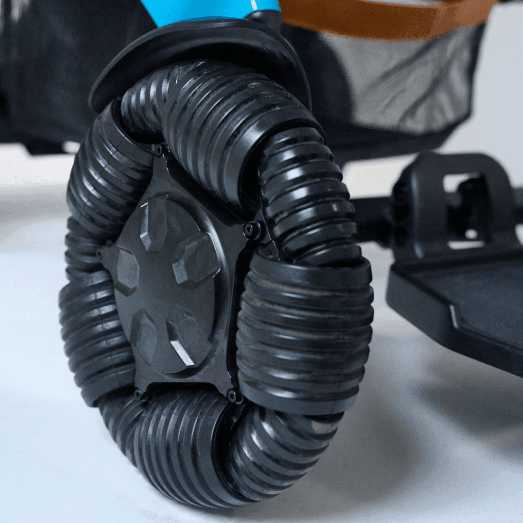Close-up of a unique black omni-directional wheel with ribbed rollers on the Ally Pro - Power Wheelchair by Golden, highlighting part of the frame and footrest for enhanced mobility and easy transport.