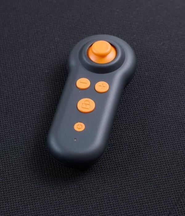 The Ally - Power Wheelchair by Golden features a compact black remote with orange buttons, a large joystick, and four smaller buttons, pictured resting on a textured black surface.