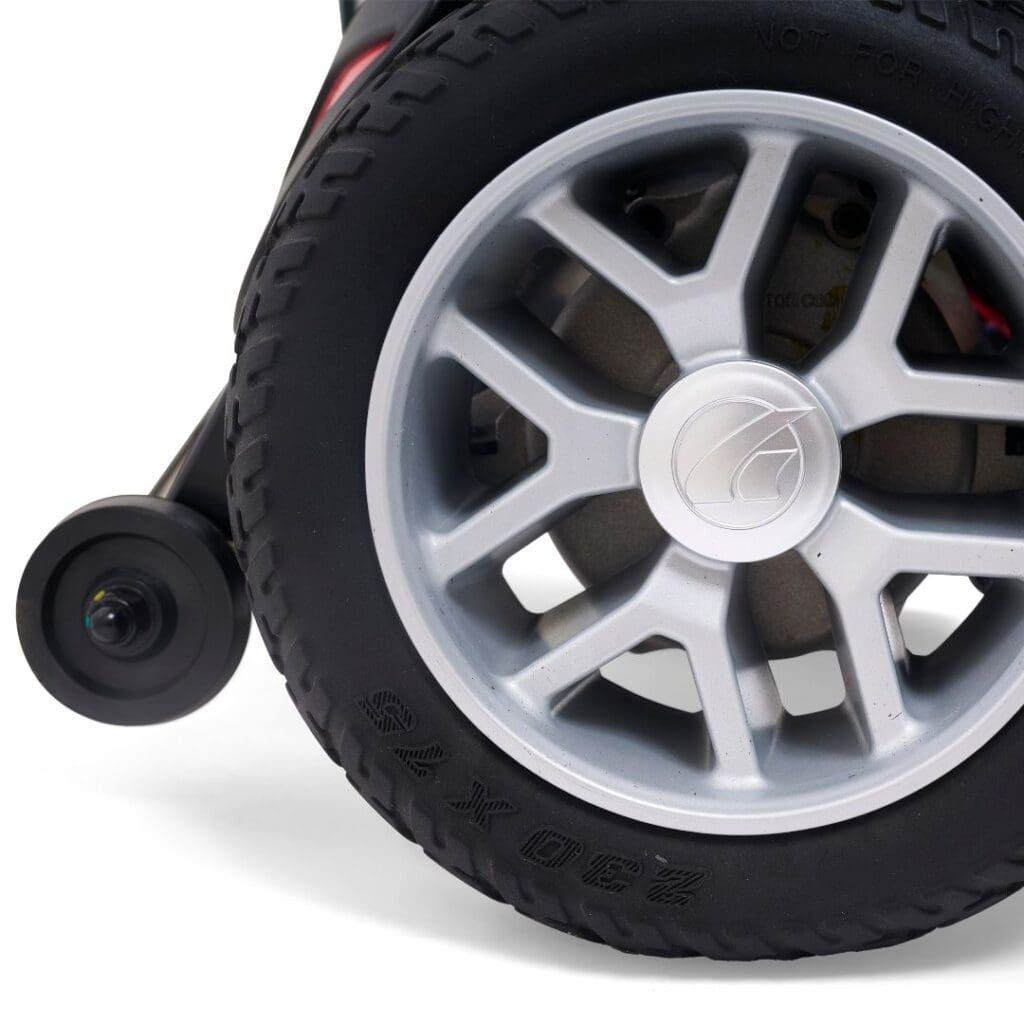 Close-up of a black rubber tire with a silver alloy wheel attached to the BuzzAbout - Power Wheelchair by Golden, featuring a small rear wheel and side-mounted camera.