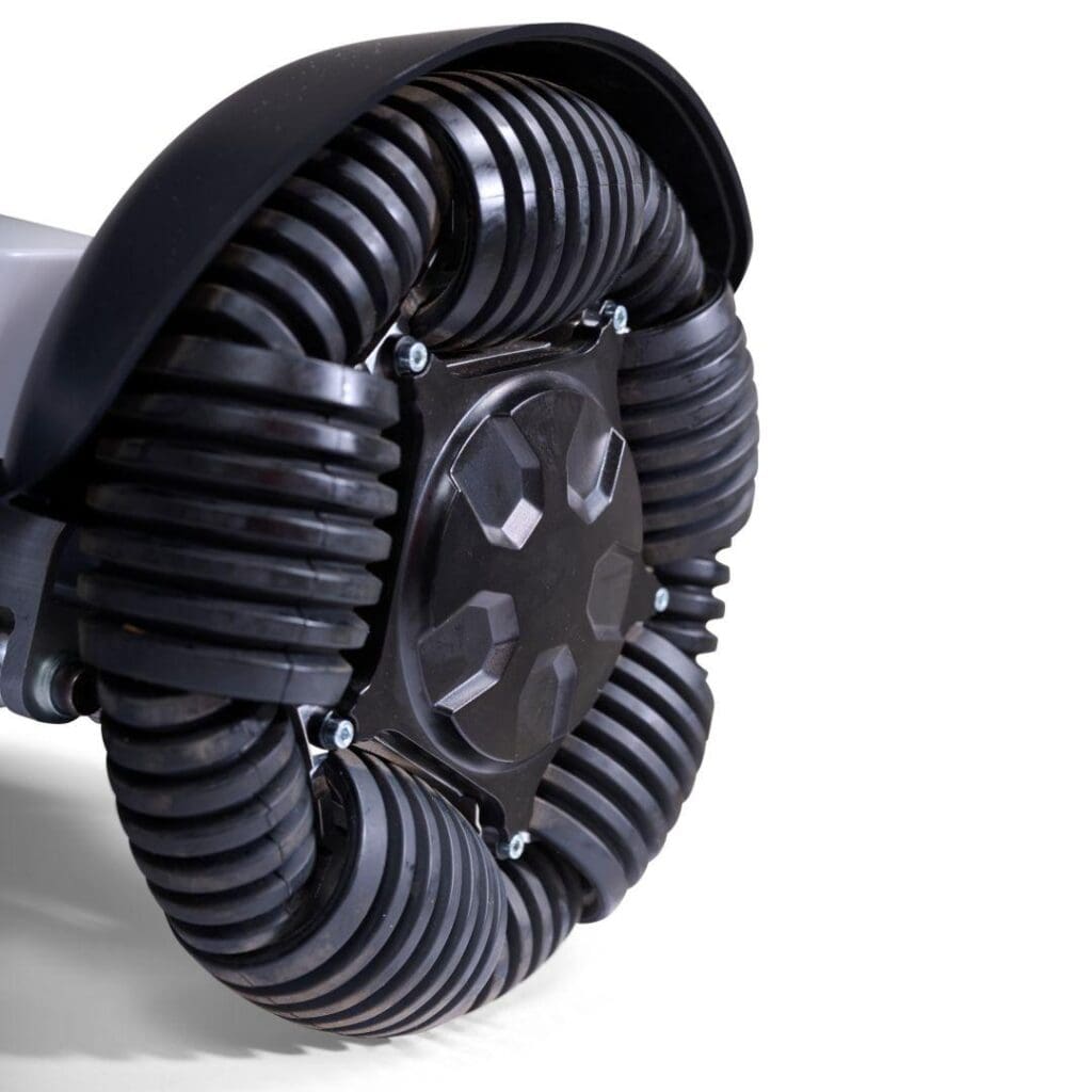 Close-up of a black omnidirectional wheel with segmented rollers, allowing multi-directional movement, attached to an Ally Sport - Power Wheelchair by Golden against a white background.