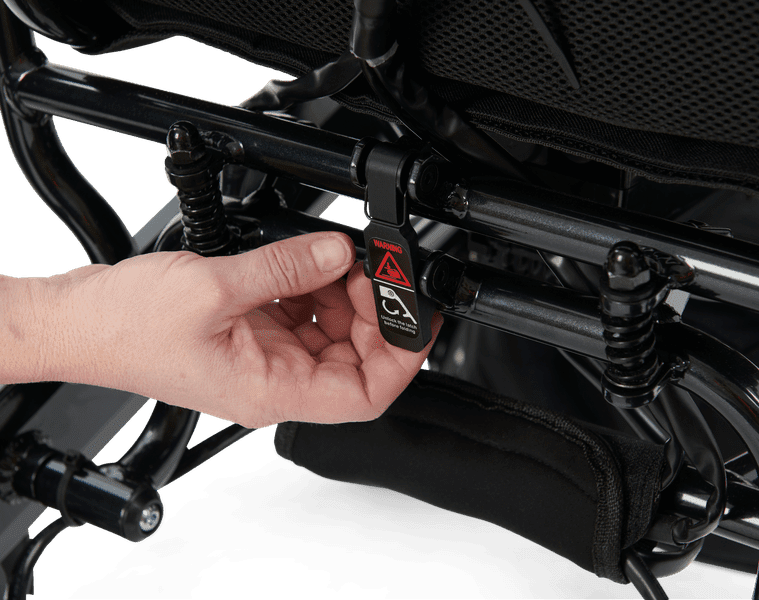 A hand adjusts the black suspension under the Stride - Power Wheelchair by Golden seat, turning a labeled dial or lever to customize ride comfort.