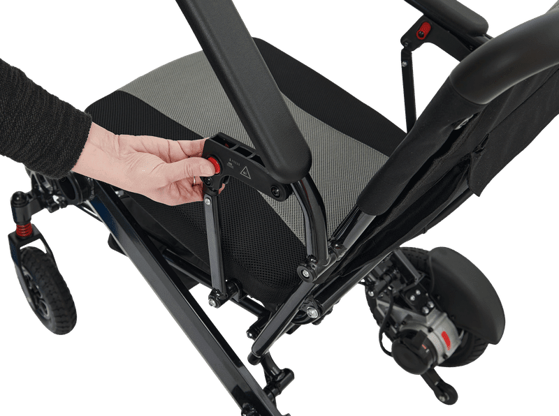 A close-up of a person pressing a red button on the frame of the black and gray Stride - Power Wheelchair by Golden, highlighting its adjustable folding mechanism.