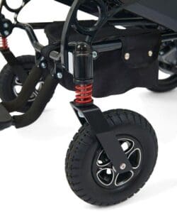 Close-up of the Stride - Power Wheelchair by Golden wheel, highlighting its black tire with five-spoke rim, red suspension spring, and part of the frame—details reminiscent of a stroller—set against a white background.