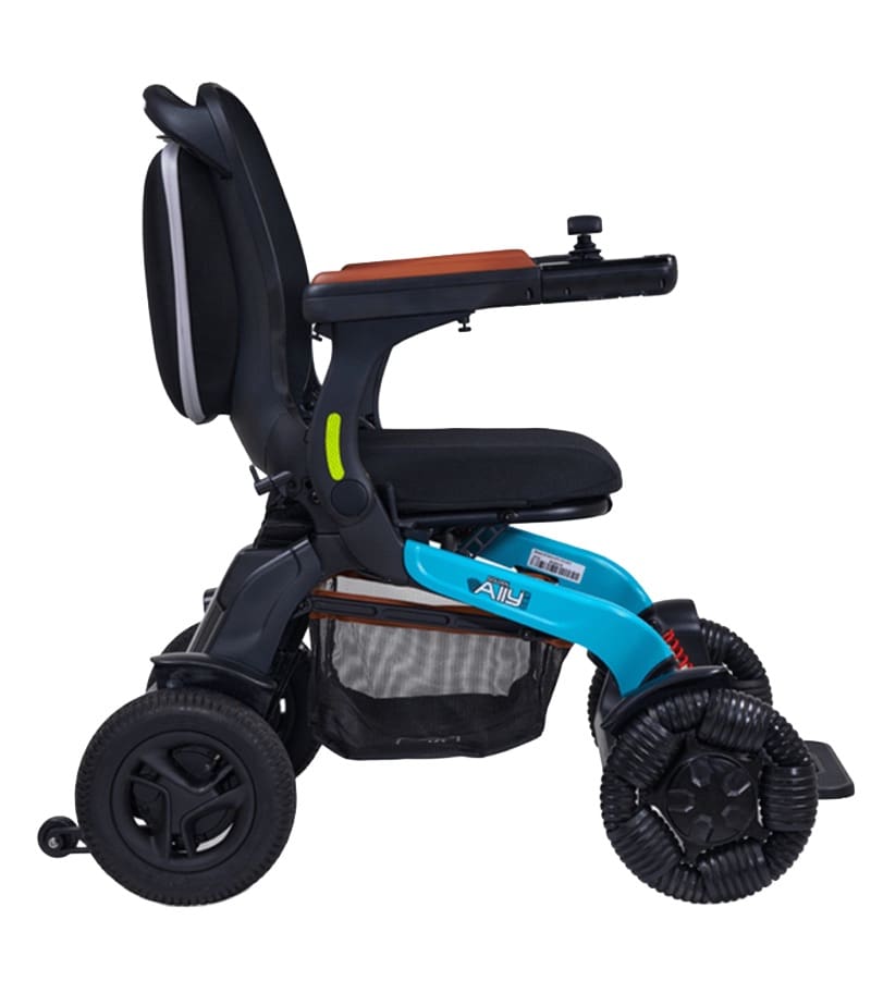Side view of the Ally Pro - Power Wheelchair by Golden: a modern, compact, foldable travel wheelchair featuring a black seat, blue frame, joystick on the armrest, distinctive wheels, and an under-seat storage basket. Side view of the Ally Pro - Power Wheelchair by Golden: a modern, compact, foldable travel wheelchair featuring a black seat, blue frame, joystick on the armrest, distinctive wheels, and an under-seat storage basket.