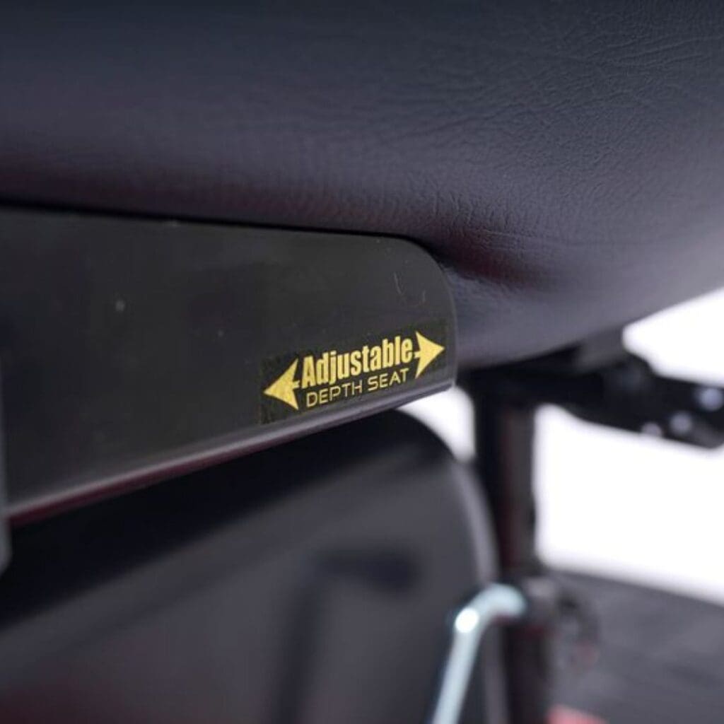 Close-up of a black seat with a yellow Adjustable Depth Seat label and arrows, highlighting customizable comfort on the Compass HD - Power Wheelchair by Golden.