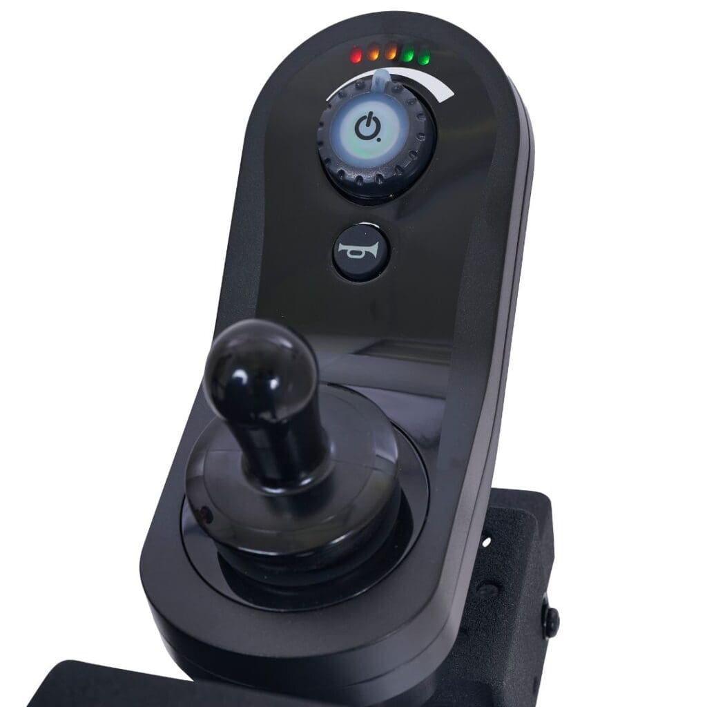 A close-up of the black electronic joystick control panel on the Compass HD - Power Wheelchair by Golden shows a power button, circular dial, battery indicator lights, and a large joystick handle mounted on a dark surface.