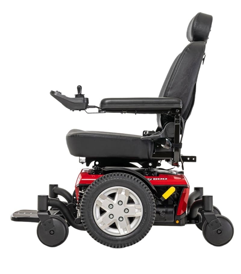A side view of the Jazzy 600 ES Power Wheelchair by Pride Mobility in red and black, featuring a padded seat, backrest, armrests, headrest, joystick controller, large rear wheels, and smaller front wheels. A side view of the Jazzy 600 ES Power Wheelchair by Pride Mobility in red and black, featuring a padded seat, backrest, armrests, headrest, joystick controller, large rear wheels, and smaller front wheels.