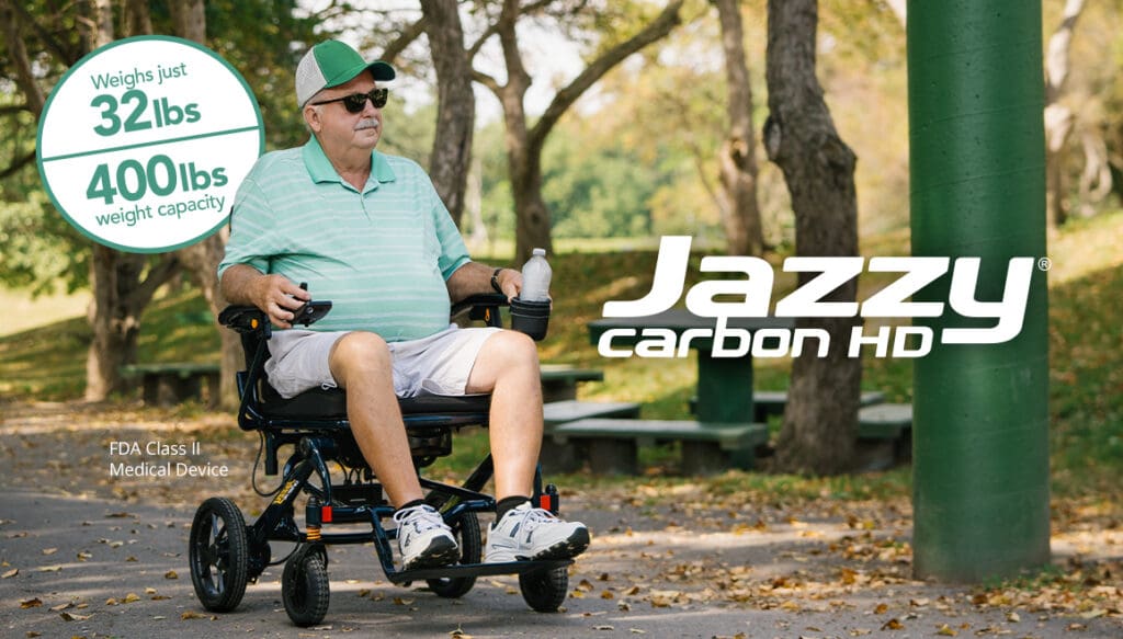 An older man in a green cap and sunglasses sits in a Jazzy Carbon HD Power Wheelchair by Pride Mobility on a park path. Text: Weighs just 32 lbs, supports up to 400 lbs, FDA Class II Medical Device.