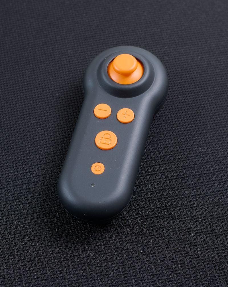 A black remote with orange buttons, including joystick, plus, minus, lock, and power symbols for the Ally Sport - Power Wheelchair by Golden, is shown on a dark textured surface.