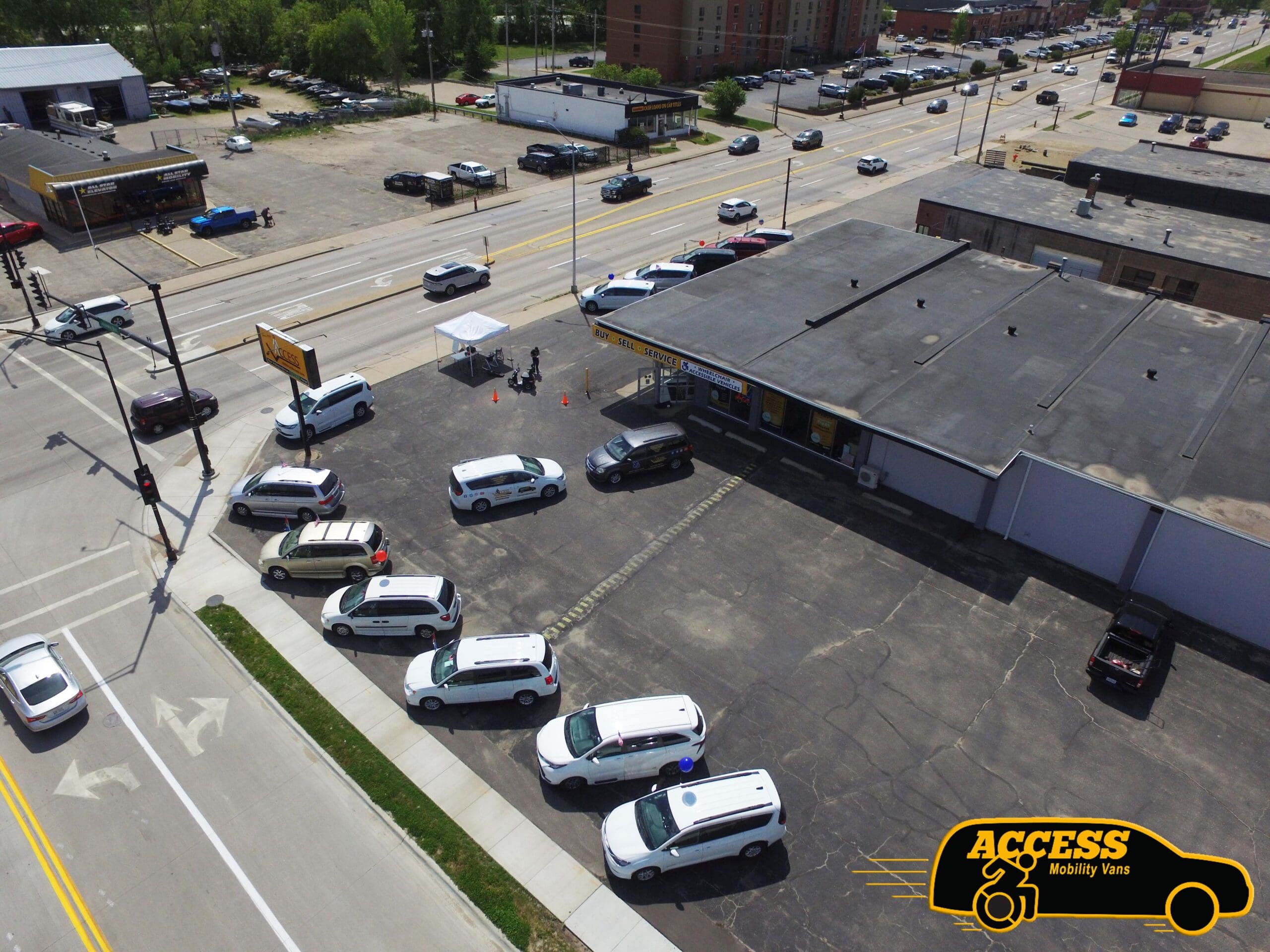 Aerial view of several white vans parked in a lot outside a building labeled Access Mobility Vans, near a main road with light traffic and nearby businesses.