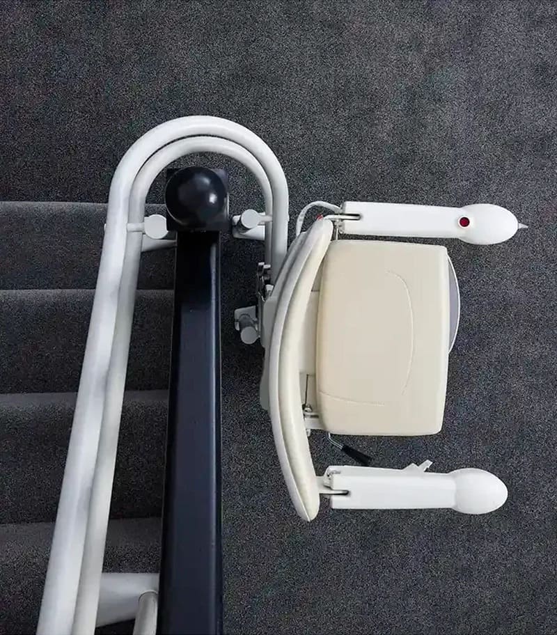 Top-down view of a beige Handicare 4000 Curved Stair Lift by Handicare mounted on a rail along a carpeted staircase, designed to safely assist individuals moving up and down stairs.