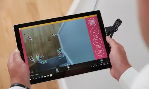 A person holds a tablet showing an augmented reality view of stairs with virtual markers—ideal for visualizing where the Stairfriend 23 Curved Stair Lift by Handicare could be installed in a home.