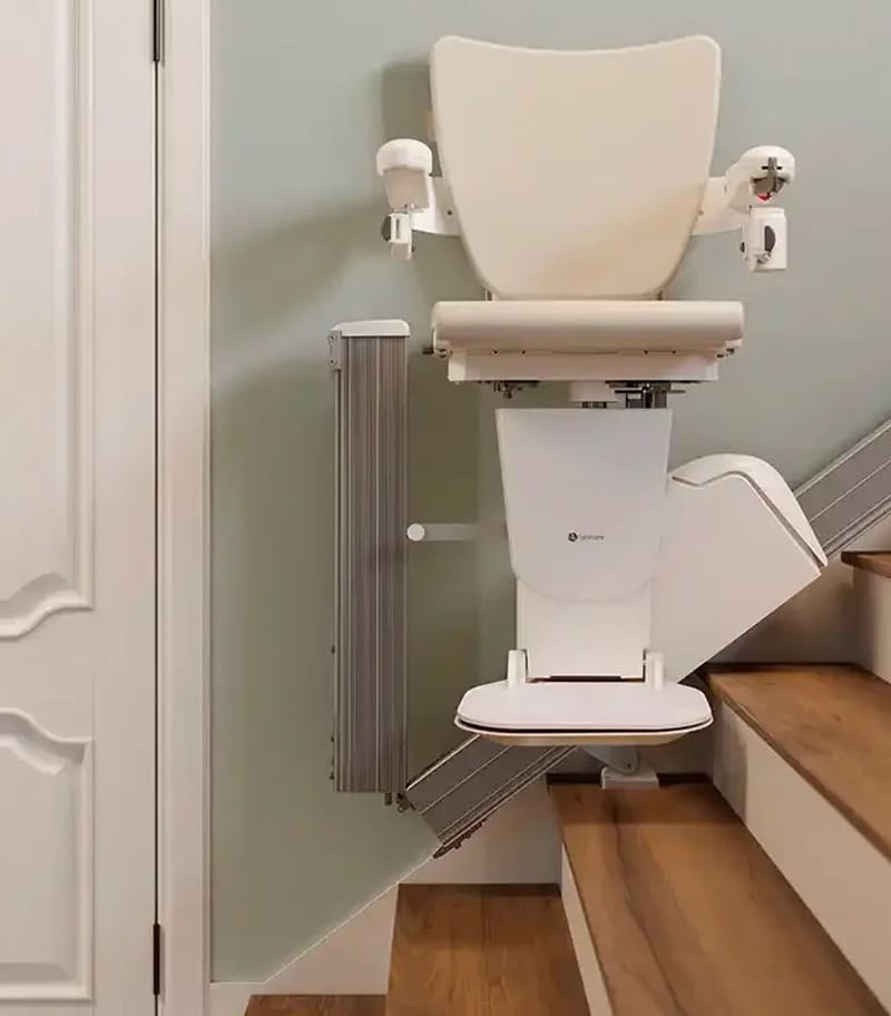 A Handicare 1100 Straight Stair Lift by Handicare is fitted to a wooden staircase beside a pale green wall and white door, offering accessible mobility support for users with physical challenges. A Handicare 1100 Straight Stair Lift by Handicare is fitted to a wooden staircase beside a pale green wall and white door, offering accessible mobility support for users with physical challenges.