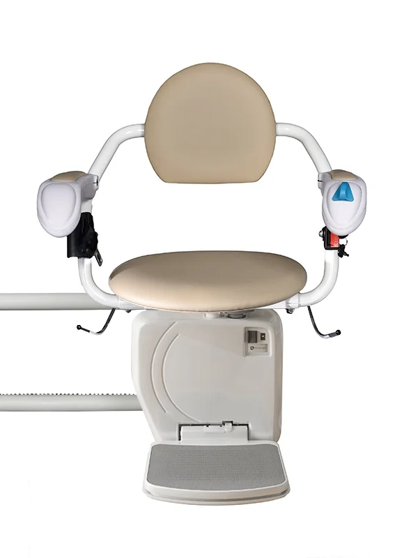 The Stairfriend 23 Curved Stair Lift by Handicare, in beige and white, features armrests, a cushioned seat and backrest, footrest, and control buttons to assist users with mobility issues on curved stairs at home.