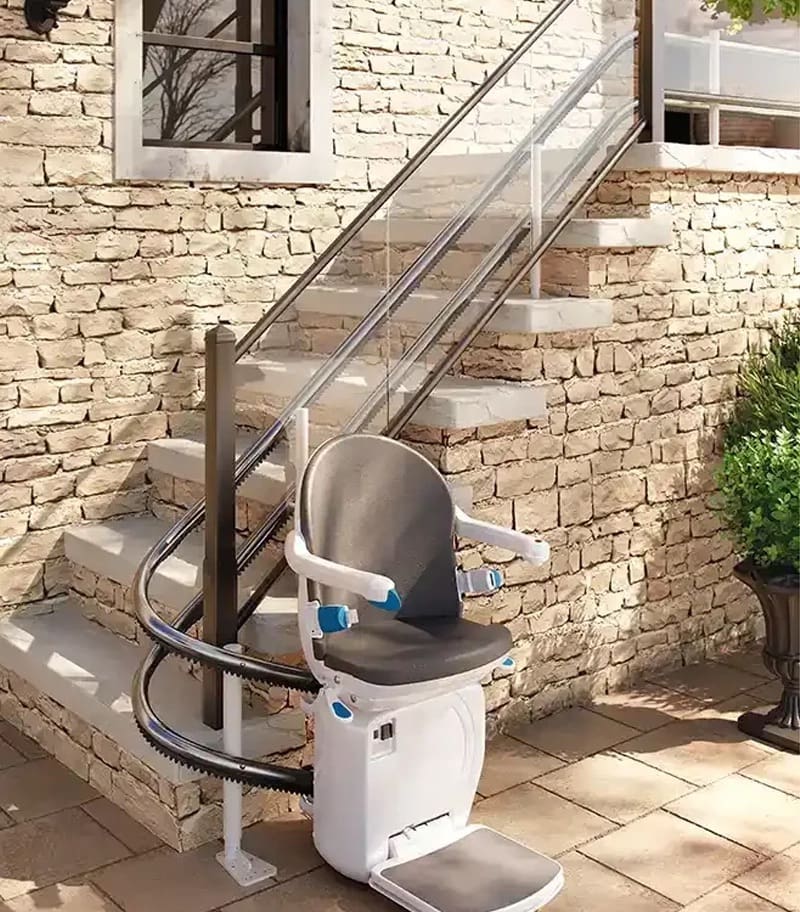 A Handicare 4000 Curved Stair Lift by Handicare is installed on an outdoor stone staircase by a brick wall, with the chair ready at the bottom for smooth, reliable transport along the curved rail for easy residential access.