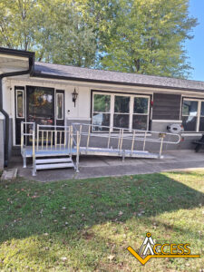 A metal wheelchair ramp with handrails leads to the entrance of a single-story house with white walls and large windows. The ACCESS company logo is visible in the lower right corner.