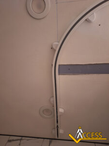 Ceiling view with a curved white track, circular recessed lights, and the Access logo in the bottom right corner. The ceiling also has some visible seams and a marble-patterned edge.