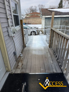 A wooden wheelchair ramp leads from a house door to a metal ramp section with snow outside. A car is parked nearby, and there is a yellow Access logo in the bottom right corner.