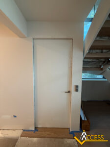 A plain white door with a silver handle is set in a white wall next to a staircase. Natural light comes in through a window above the stairs. The Access company logo is in the bottom right corner.