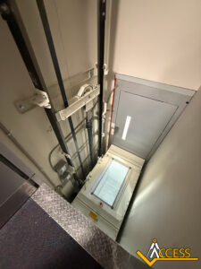 View from above of an open shaft for a vertical platform lift. The mechanical components and rails are visible, with the Access company logo in the bottom right corner. The lift platform is at the lower level.