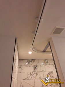 Ceiling view of a bathroom with marble-patterned walls, a curved track for a curtain, a recessed light, and a vent. The Access logo is in the bottom right corner.