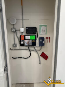 Small electrical and control panel closet with various electrical boxes, exposed wiring, warning labels, and four red fuses on the wall. The ACCESS logo is in the bottom right corner.
