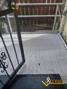 View from an open door looking out onto a small, white, corrugated ramp with a metal railing, leading to a fenced yard. The Access company logo is visible in the lower right corner.