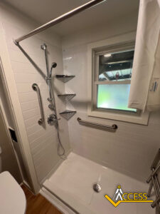 A walk-in shower with white tile walls, a handheld showerhead, grab bars, corner shelves, a small window, and a curtain rod. The Access logo is visible in the bottom right corner.