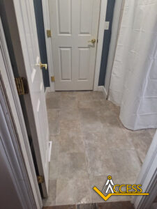 A bathroom with light-colored tile flooring, blue-gray walls, a white door, a shower with a white curtain, and the Access logo in the bottom right corner.