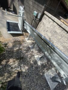 A motorized lift platform on a metal track is installed beside a stone wall on a gravel path, leading up to a higher level near a building.