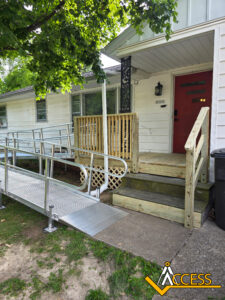 A house with a red door has a wooden porch with stairs and a metal wheelchair ramp for accessibility. There is a tree providing shade and the word ACCESS is in the bottom right corner.