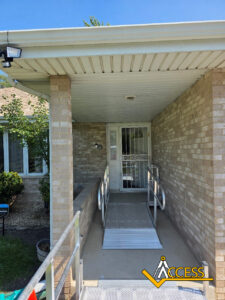 A house with a ramp leading to the front door, providing wheelchair access. The door has a security screen, and there is a camera above the entryway. The ACCESS logo is at the bottom right corner.