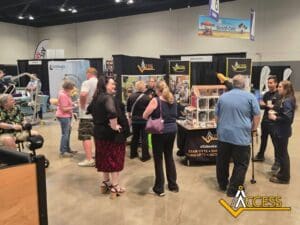 A group of people gathers around the Access exhibit booth at an indoor convention, engaging with staff and displays about stair lifts, ramps, and accessibility products. The Access logo is visible in the corner.