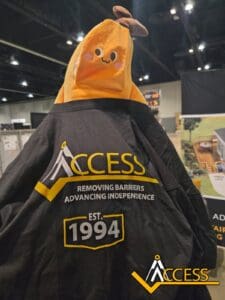 A plush banana toy wears a black ACCESS shirt with the slogan “REMOVING BARRIERS ADVANCING INDEPENDENCE” and “EST. 1994.” ACCESS logos are visible on both the shirt and bottom right of the image.