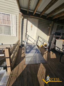 A metal wheelchair ramp leads up to a white door on a wooden porch attached to a beige house. The ACCESS logo is visible in the bottom right corner of the image.
