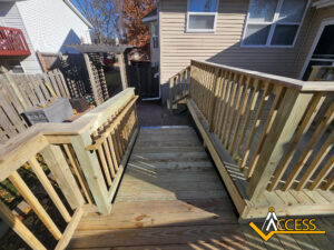 A wooden wheelchair-accessible ramp leads from a porch to a backyard with a wooden fence. A pergola and storage bins are visible on the left. The Access logo is in the bottom right corner.