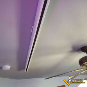 A white motorized curtain track is installed on a light-colored ceiling, near a ceiling fan and a smoke detector. The Access logo is visible in the bottom right corner.