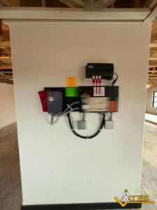 A fire alarm control panel and related electrical equipment mounted on a white wall in a commercial building under construction, with exposed ceiling beams and the Access company logo in the bottom right corner.