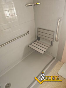 Accessible shower with grab bars on the walls and a fold-down shower seat. The floor is flat and level with the bathroom, and the ACCESS logo is visible in the corner.