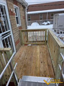 A small wooden porch with railings attached to a brick building, accessed by a metal ramp. Snow is visible on the ground and rooftops in the background. The ACCESS company logo is at the bottom right corner.
