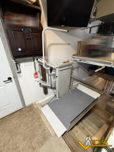 A vertical platform lift is installed in a garage, providing wheelchair access. The lift is positioned next to a door and cabinetry, with a ramp for easy entry. The Access company logo is visible in the bottom right corner.