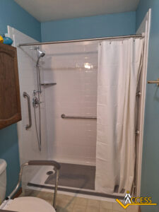 A walk-in shower with a white curtain, wall-mounted grab bars, a handheld showerhead, shower chair, and light blue walls. The ACCESS logo is in the bottom right corner.