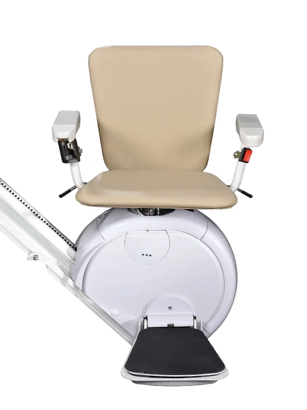 Front view of a Savaria K2 stairlift with the optional L seat, featuring a beige padded seat and full backrest, white armrests with integrated controls, a white carriage housing, and a black foldable footrest. The stairlift is mounted on a straight rail and displayed against a white background, showcasing its supportive seating design and compact profile.